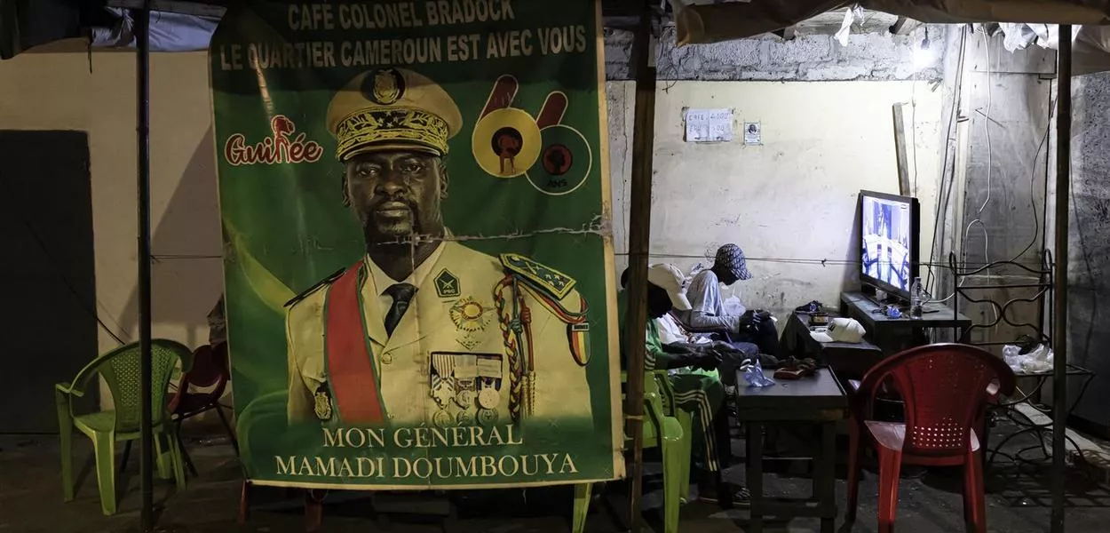 Residents watch television next to a poster depicting Guinea President Mamady Doumbouya ahead of the announcement of provisional official referendum results in Conakry, on September 23, 2025. Guinea's junta leader General Mamady Doumbouya officially entered his country's presidential race on November 3, 2025, submitting his candidacy to the Supreme Court ahead of December 28 elections that are meant to restore constitutional order following a 2021 coup. (Photo: Patrick Meinhardt/AFP)